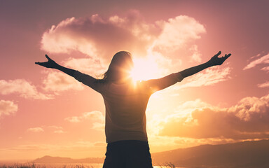 Happy young female with arms up to the sunset sky feeling inspired and free in a beautiful nature...