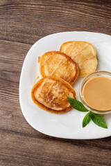 Pile of freshly fried thick pancakes, in Eastern European cuisines called oladky or oladyi with condensed milk on wooden background