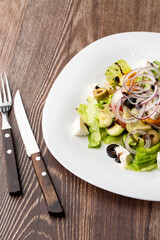 Greek salad with fresh vegetables: tomato, cucumber, red bel pepper, lettuce, onion, olives and cheese. Close-up on a wooden background.