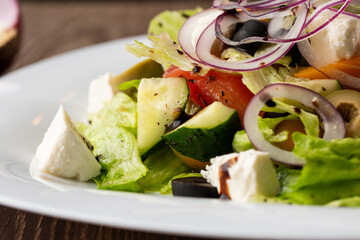 Greek salad with fresh vegetables: tomato, cucumber, red bel pepper, lettuce, onion, olives and cheese. Close-up on a wooden background.