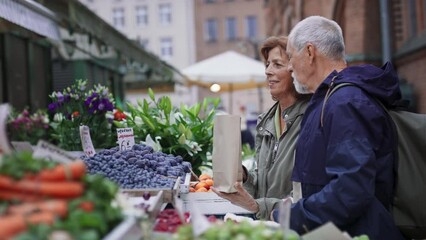 Happy senior couple tourists buying fruit outdoors on market in town. - Powered by Adobe