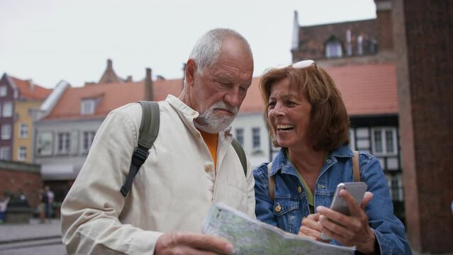 Happy senior couple tourists using smartphone and map outdoors in historic town