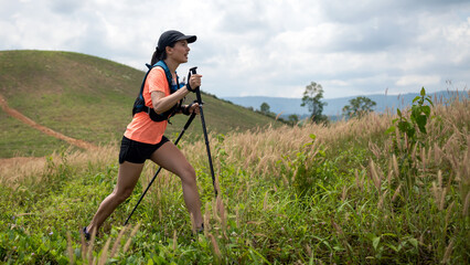Young women active trail running across a meadow on a grassy trail high in the mountains in the...
