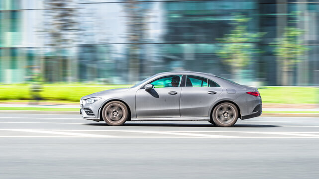 Side view rolling shot with gray car in motion. Mercedes CLA Class driving along the street in city with blurred background