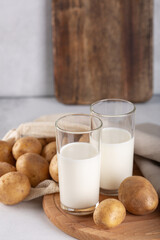 Vegan plant based milk in two transparent glasses. Alternative potato milk and potato tubers on gray table