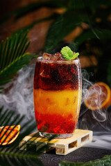 Bumble coffee with ice on a dark tropical background. Espresso, orange juice and syrup in layers in transparent glass with ice. Summer trendy refreshing coffee drink. Coffee house menu, recipe. Copy