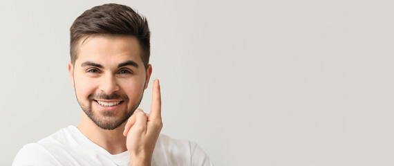 Handsome young man holding contact lens on light background with space for text