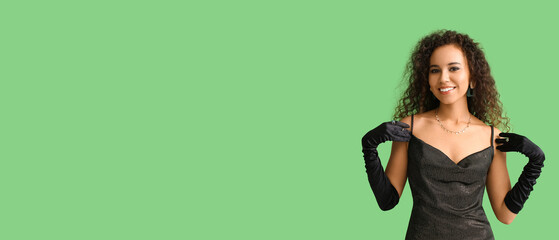 Fototapeta na wymiar Elegant young African-American woman in beautiful dress and gloves on green background with space for text