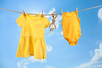 Baby clothes and toy hanging on rope against blue sky