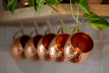 Copper Moscow Mule mugs hanging from kitchen shelves as decor.