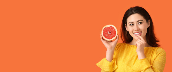 Beautiful smiling young Asian woman holding fresh grapefruit on orange background with space for text