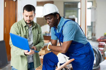 Caucasian man architect using laptop to show repair works plan to african-american foreman.