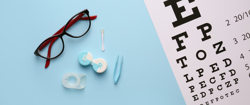 Contact lenses, eye test chart and glasses on light blue background