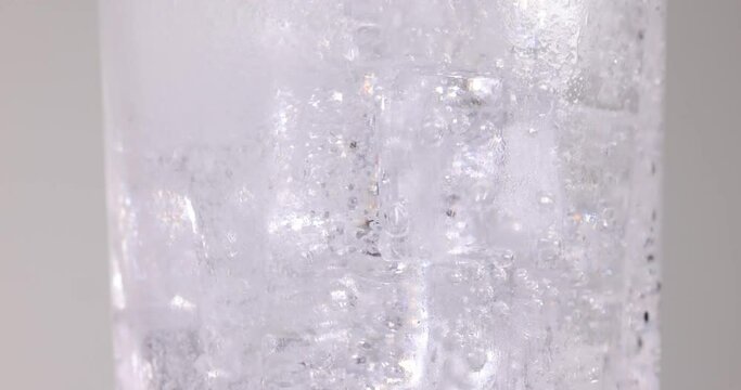 Clear transparent soda water pouring into a tall glass filled with ice fizz bubble foam floating up on white background