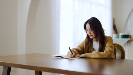 Obraz premium Beautiful young asian woman sitting and taking note at house. Happy smiling working online, Freelance work at home