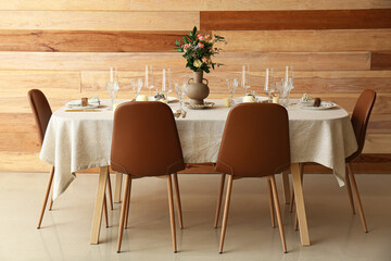 Stylish table setting with beautiful flowers near wooden wall