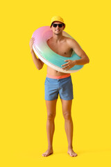 Attractive young man with inflatable ring on yellow background