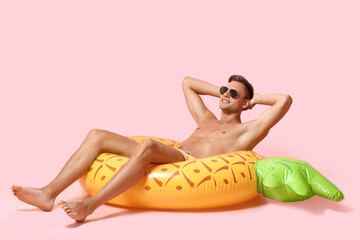 Happy young man with inflatable ring on pink background