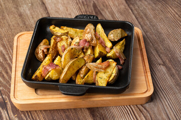 Delicious Fried Potato Bratkartoffeln With Bacon and Onion close up in the black plate on the table.