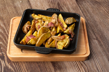 Delicious Fried Potato Bratkartoffeln With Bacon and Onion close up in the black plate on the table.