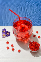 Glass of fresh pomegranate soda and flowers near swimming pool, closeup
