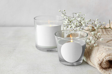 Fototapeta na wymiar Glass holders with burning candles, flowers and sweater on light background, closeup