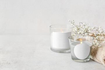 Glass holders with burning candles, flowers and sweater on light background