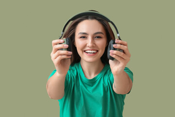 Beautiful young woman with headphones on green background