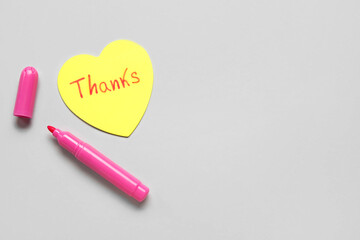 Heart shaped sticky note with word THANKS and felt-tip pen on grey background