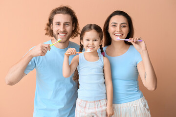 Little girl with her parents brushing teeth on beige background