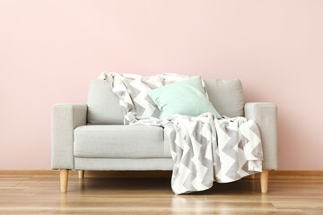 Modern sofa with pillow and plaid near color wall in room