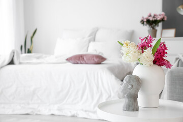 Vase with beautiful hyacinth flowers and stylish decor on table in bedroom