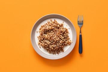 Plate of tasty buckwheat porridge on orange background, top view