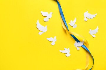 Ribbon in colors of Ukrainian flag and heart made of paper doves as symbol of peace on yellow...