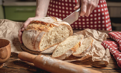 Hands cut with a knife homemade natural fresh bread with a Golden crust on wooden background. Baking bakery products