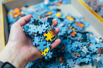 The hand holds the puzzles. A box with puzzles. A home hobby. A picture of puzzles, pieces. Cardboard box.