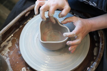 Women hands on a potter  wheel sculpt a pot in the shape of a heart