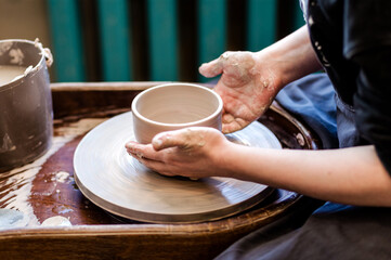 close up hand modeling pottery on a potter wheel in a cozy home workshop.