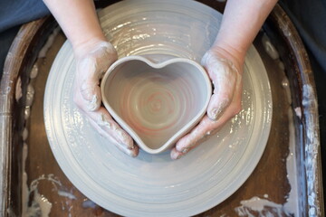 Women hands on a potter  wheel sculpt a pot in the shape of a heart - Powered by Adobe