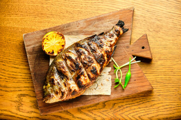 Big fish dorado with lemon and sauce on wooden table in luxury restaurant