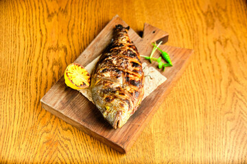 Big fish dorado with lemon and sauce on wooden table in luxury restaurant