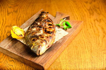 Big fish dorado with lemon and sauce on wooden table in luxury restaurant