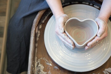 Close-up of female hands, making the shape of a heart from a bowl on a potter wheel