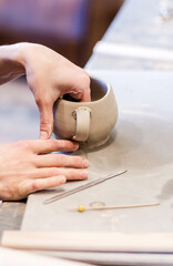 Creative female master sitting by table in her studio and moulding mug from soft grey clay