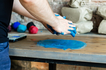 Male hands is mixing blue dye with clay on a wooden table.