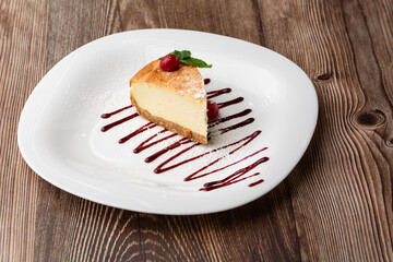 Cheesecake New York or classic cheesecake with caramel. Closeup view. Tasty breakfast. Piece of cake on white plate, on wooden background.