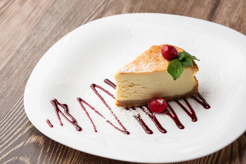 Cheesecake New York or classic cheesecake with caramel. Closeup view. Tasty breakfast. Piece of cake on white plate, on wooden background.