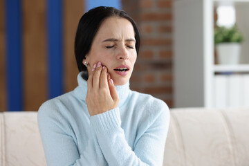 Young woman with acute toothache on couch