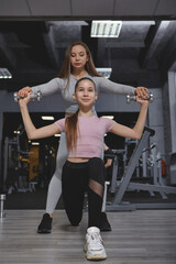 Vertical full length shot of a teen girl doing lunges with weights, personal trainer supervising the workout