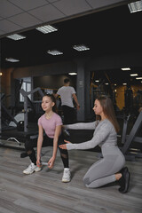 Fototapeta na wymiar Vertical full length shot of a teenage girl doing squats with weights, her personal trainer supervising